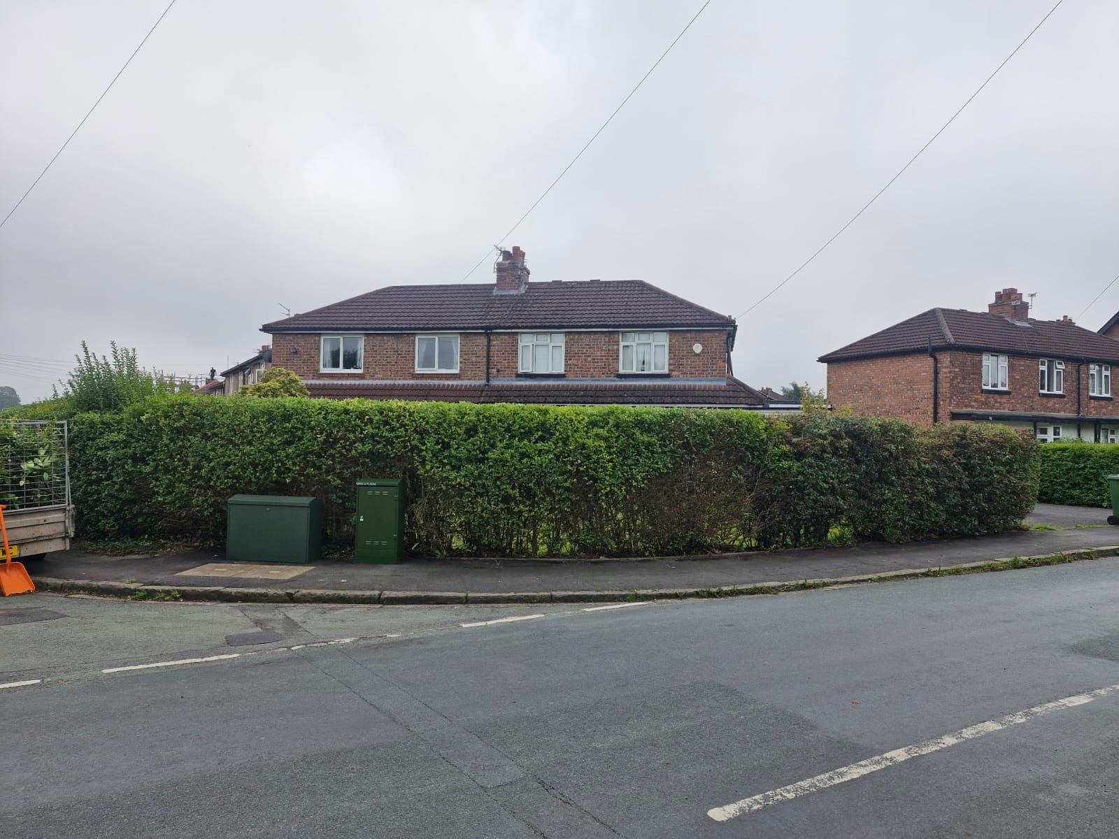 A long roadside hedge on a street corner cut back straight and level