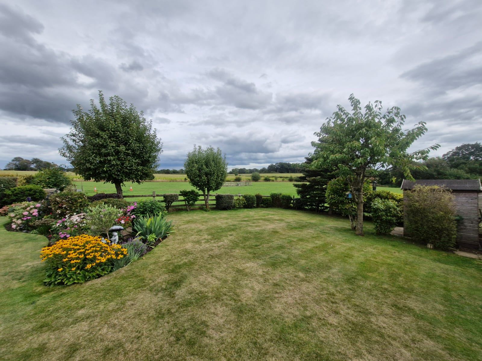 A wide country garden lawn with shaped trees and flower beds