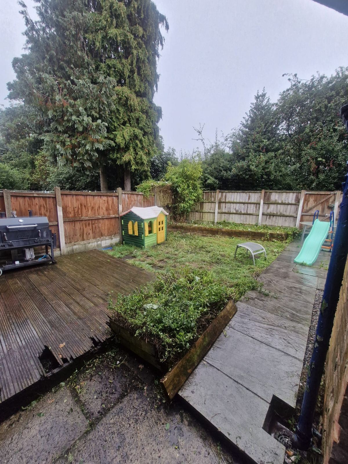 A back garden with decking and a lawn, cleared of overgrown shrubs and green waste